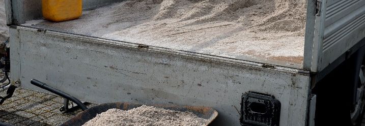 Schubkarre mit Sand steht vor einem Anhänger voller Sand